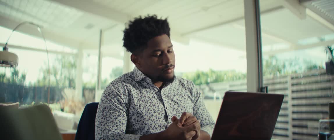 Man seated at a table looking at a laptop while adjusting his hands
