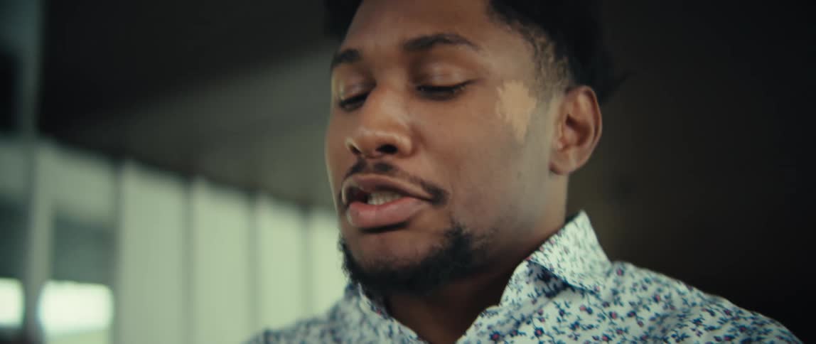 Young adult black man walking indoors and talking and smiling with a smartphone on his hand then suddenly stopping with a surprised and nervous facial expression indoors during day time