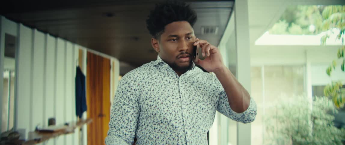 Man walks through a room with his phone in his hand listening and thinking before he speaks