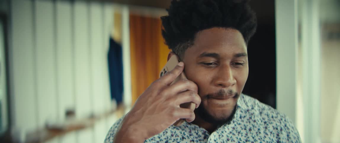 Man walks through a room with his phone in his hand listening and smiling in celebration