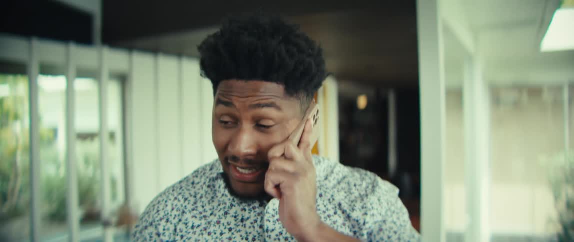 Man smiles as he stands in a room talking on his phone and pauses with a sigh of relief