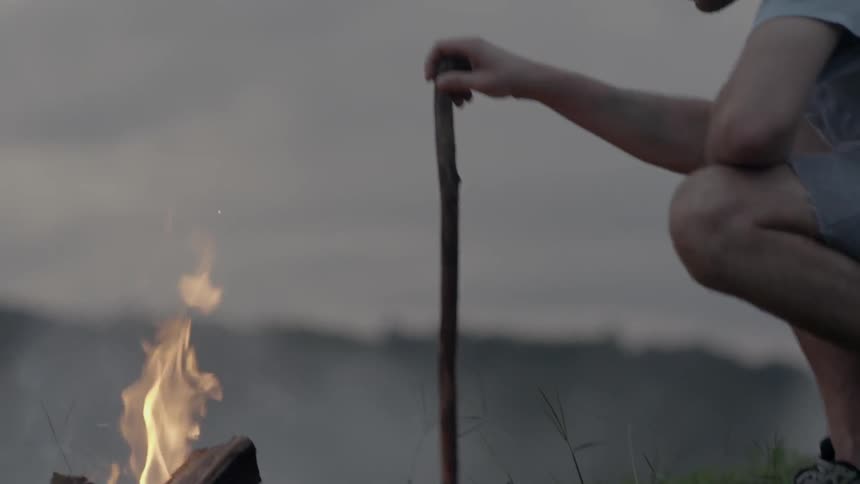 Man pokes a stick into a fire outside