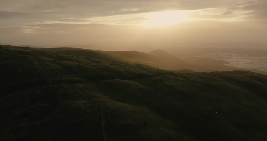 Rolling green hills under cloudy sky at sunset