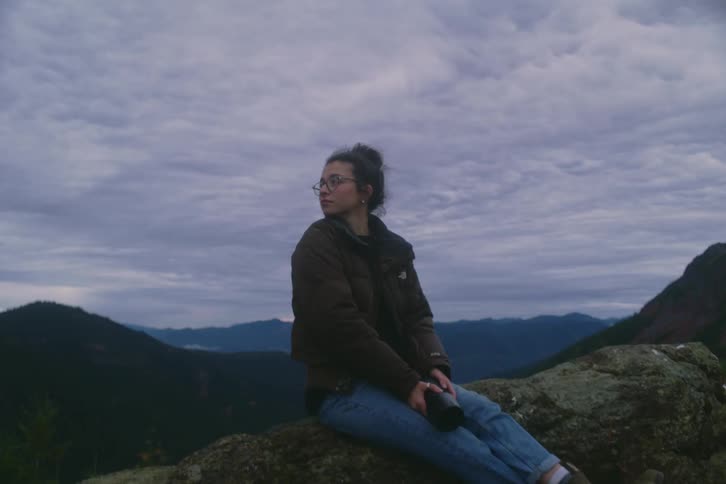 Person seated on rock facing mountain landscape