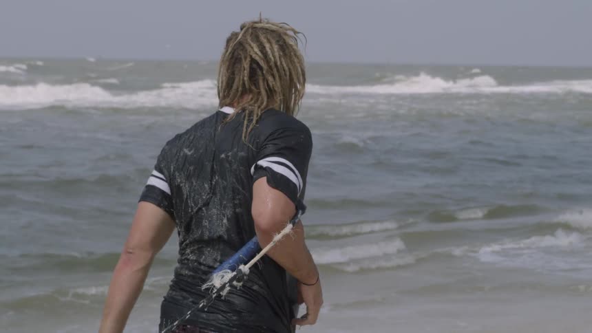 A man with a strap and rope on his arm i dragging something along the shore at the beach