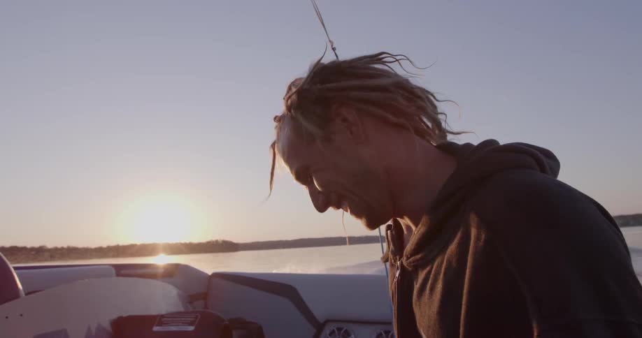Smiling man on a boat giving the thumbs up with the sun setting in the distance