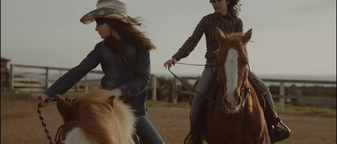 Woman wearing a hat holding reins while another rides a horse beside her