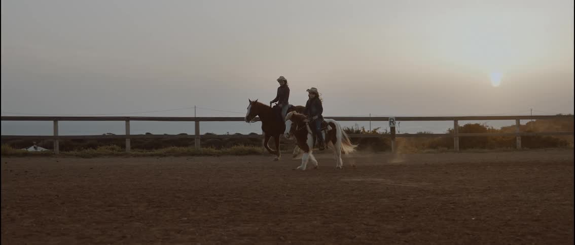 A Woman and her daughter ride horses on a ranch at sunset