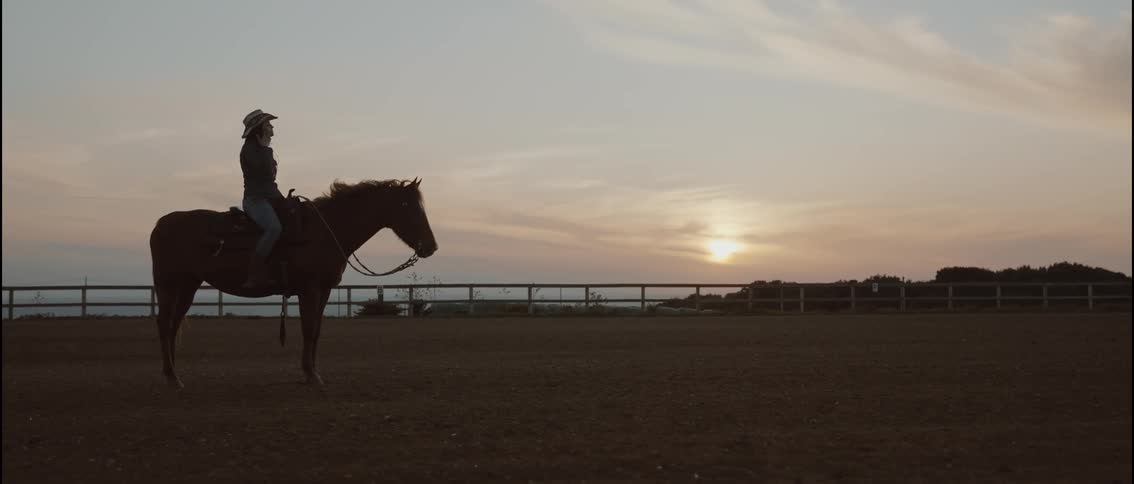 A woman sitting on a horse in an arena at sunset