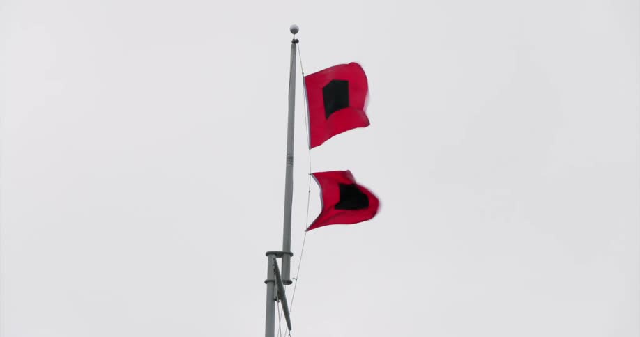 Two red flags with black square hoisted on a pole against a cloudy sky