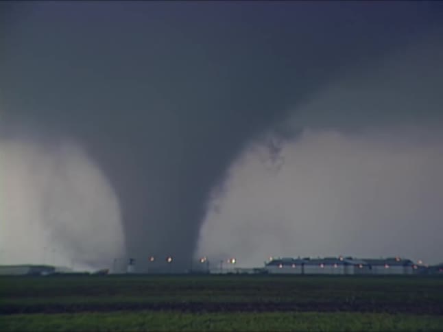 Large tornado moving across a flat area with buildings in the background