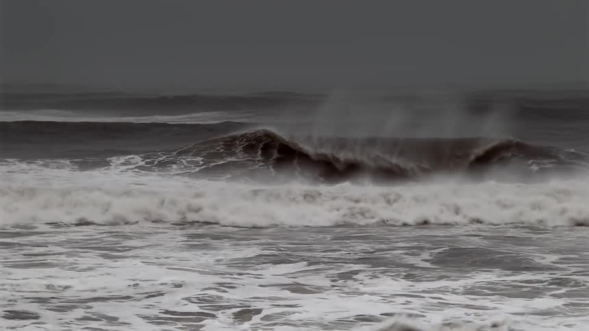 Rough water waves splash and foam as they roll in to shore under a dark sky