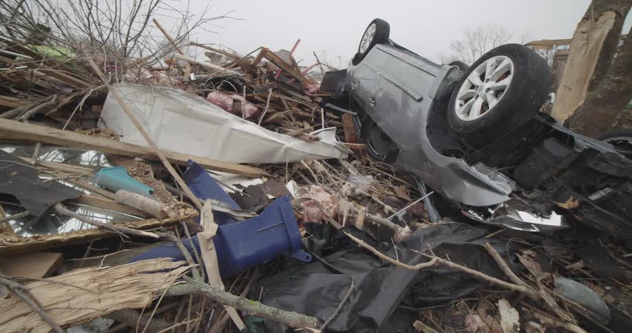 An overturned car rests on a massive pile of debris and wreckage following a destructive storm