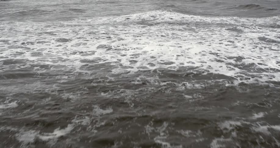 Rough water waves splash and foam as they roll in during a storm