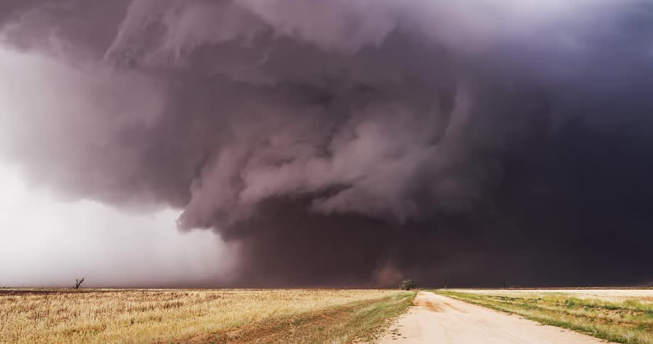 Supercell storm with dense clouds moving over open field beside a rural road