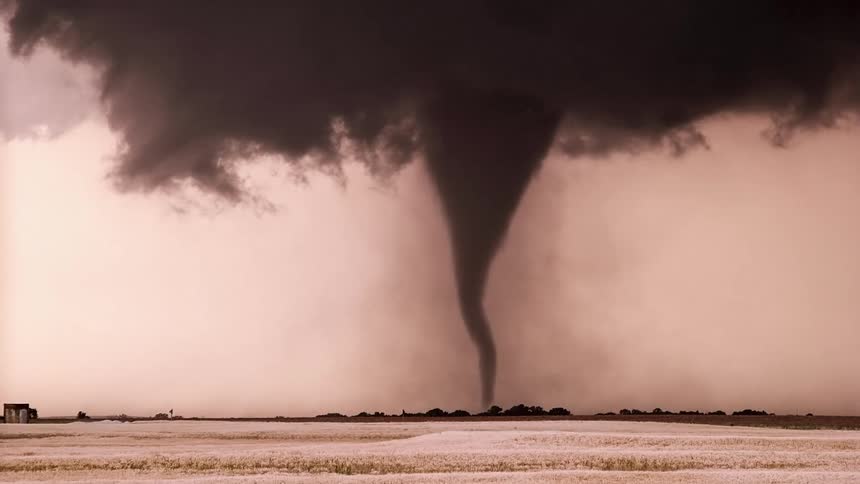 Funnelshaped tornado over open field beneath a darkened sky