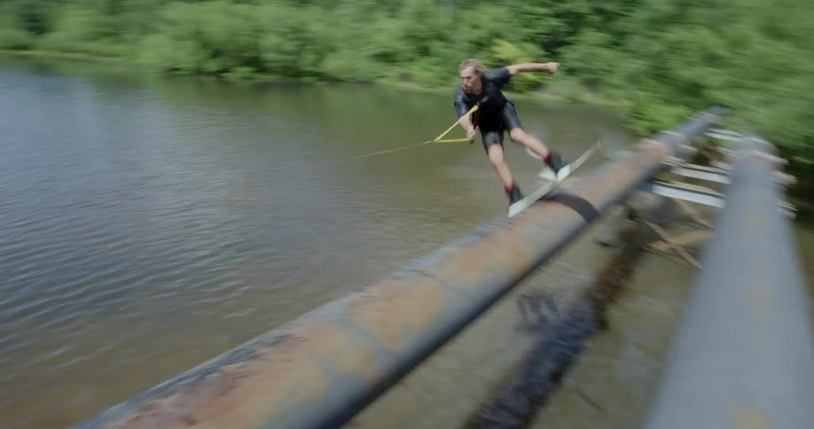 Person water skiing jumps up on a pipe and skids across it over a river and falls down