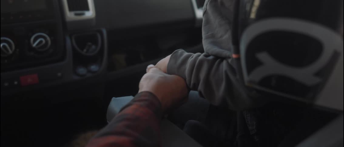 An adult man gently holds and squeezes a childs hand inside a vehicle