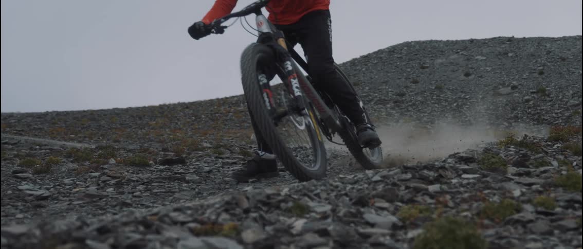 Cyclists rides a bicycle along a sloping dirt path creating a spray of gravel on an autumn day