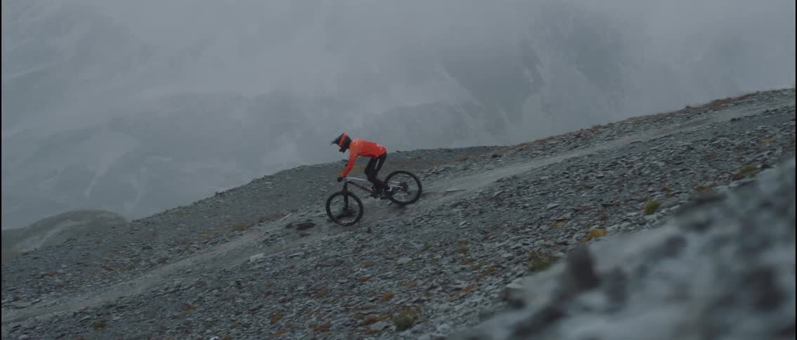 A mountain biker rides down a mountain trail on a cloudy day wearing a red helmet