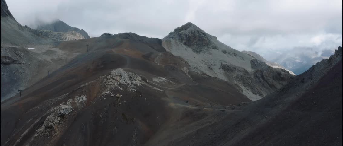 Mountain range with rocky peaks and trails under cloudy sky