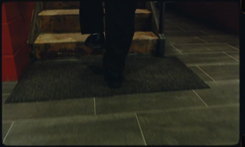 Man in dress pants and formal shoes walks across a floor that changes from tile to carpet then walks up tiled stairs