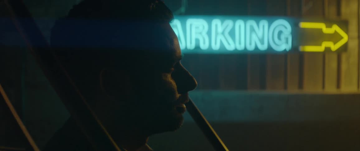 A sign glows behind a man's head at night
