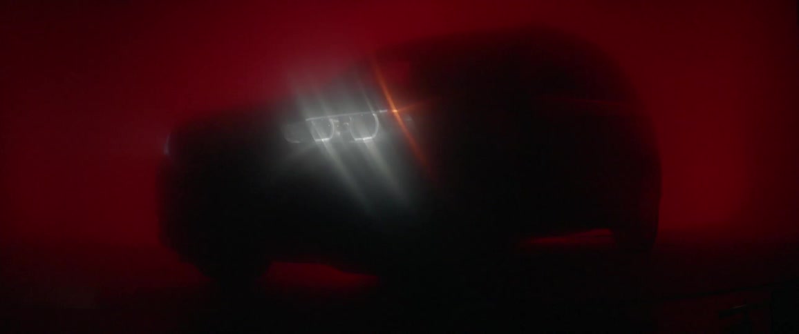 A vehicle's lights are shining and casting rays against a red background