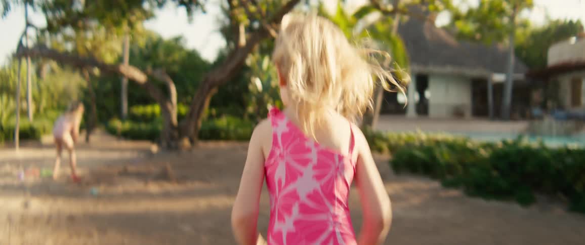 Girl in a pink swimsuit running in an outdoor area with trees and buildings in the background
