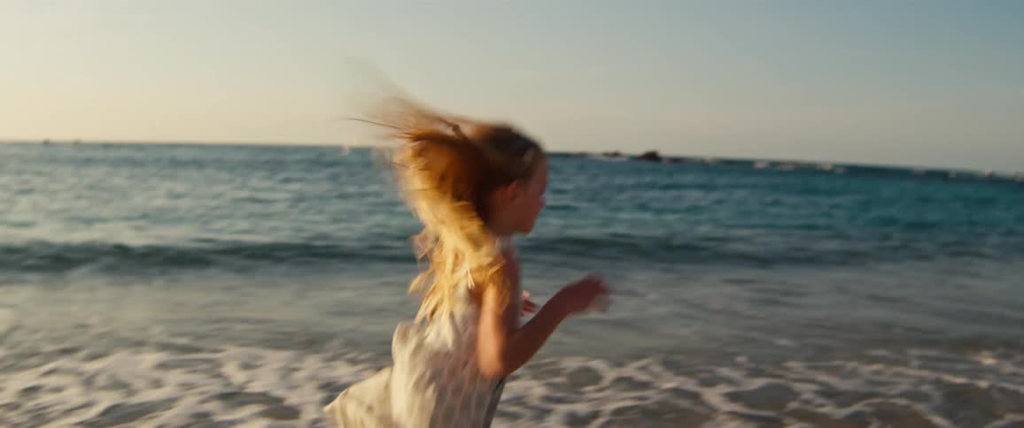 Blonde girl running along the shoreline with waves in the background