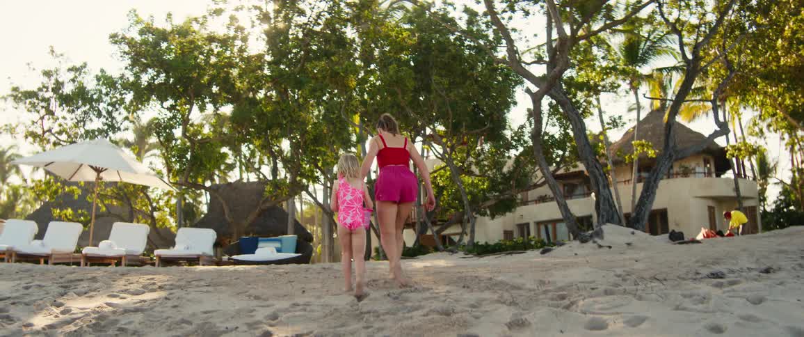 Young adult woman and female child wearing a bathing suit walking on a beach at a resort outdoors during day time
