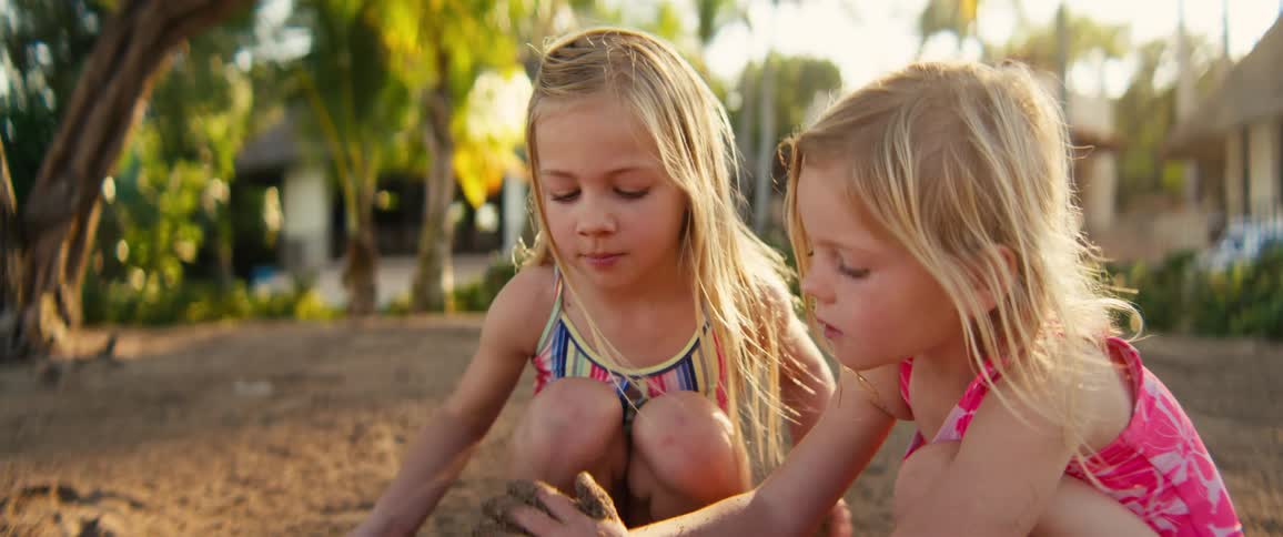 Two young girls play together with wet sand on a beach