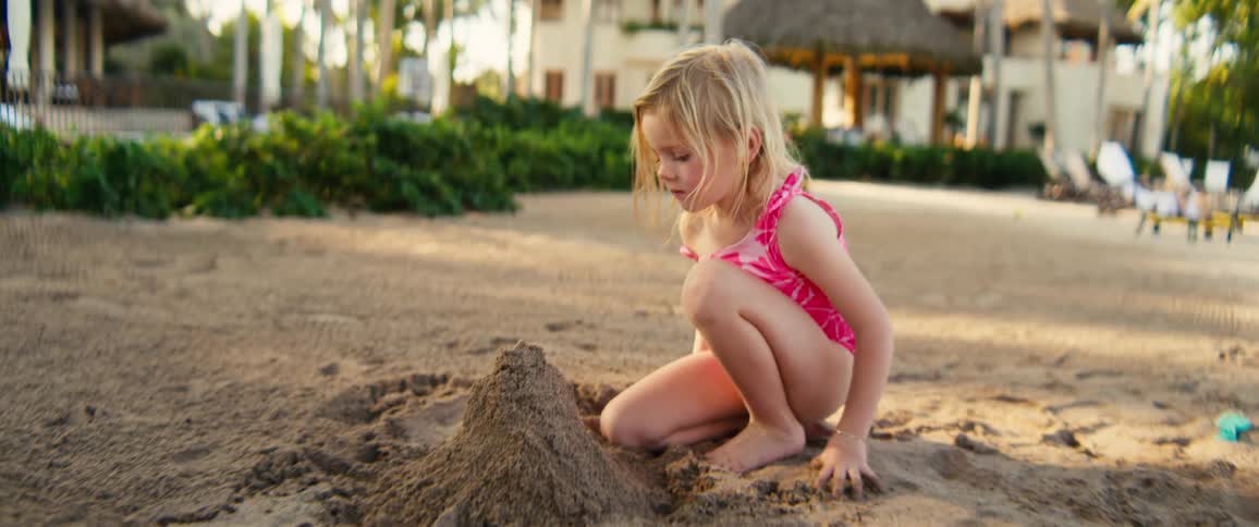 Two little girls building mounds in the sand with buildings in the distance