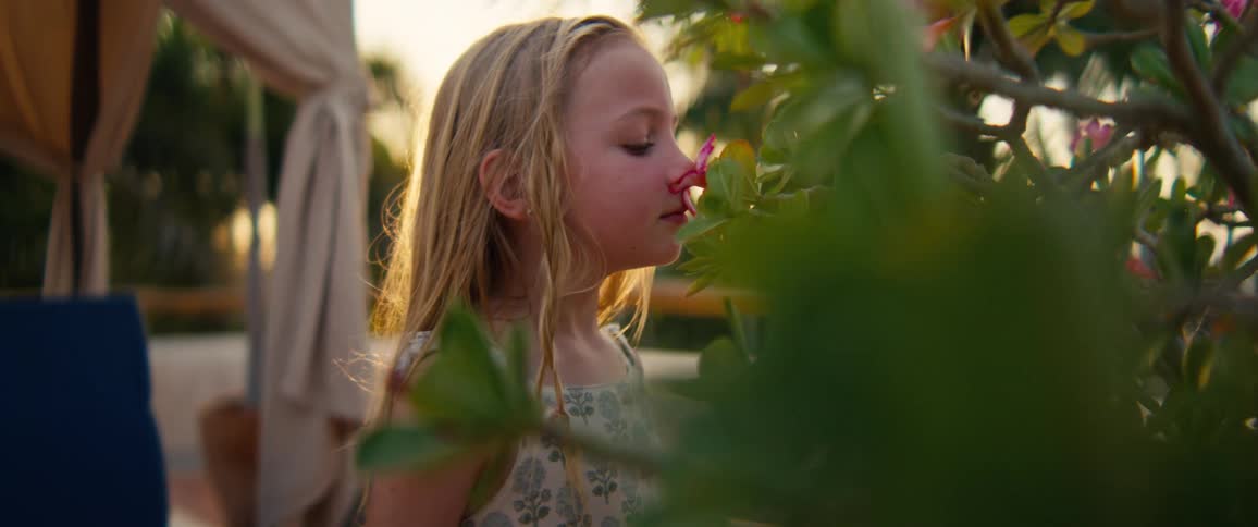 Blonde girl smelling a flower among green leaves outdoors