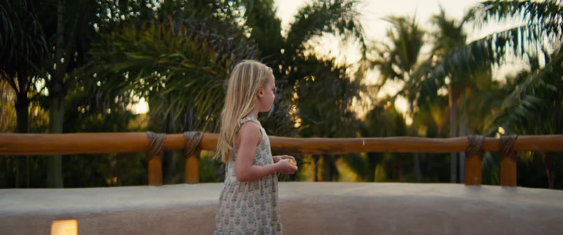 A young girls snacks while outside on a patio surrounded by palm trees