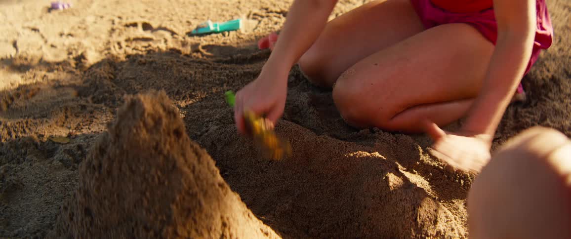 Kids shaping sand with hands on the beach at sunset