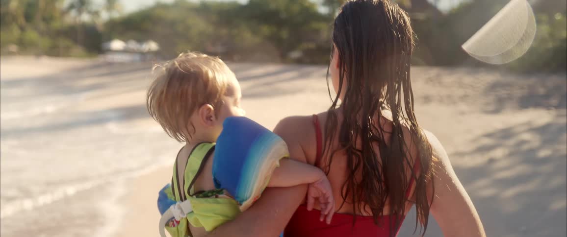 A woman carrying a baby on a beach in slow motion