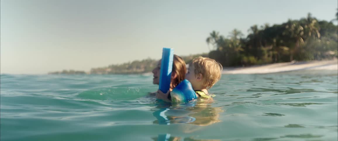 A young woman swims with her child in the ocean near the beach at midday