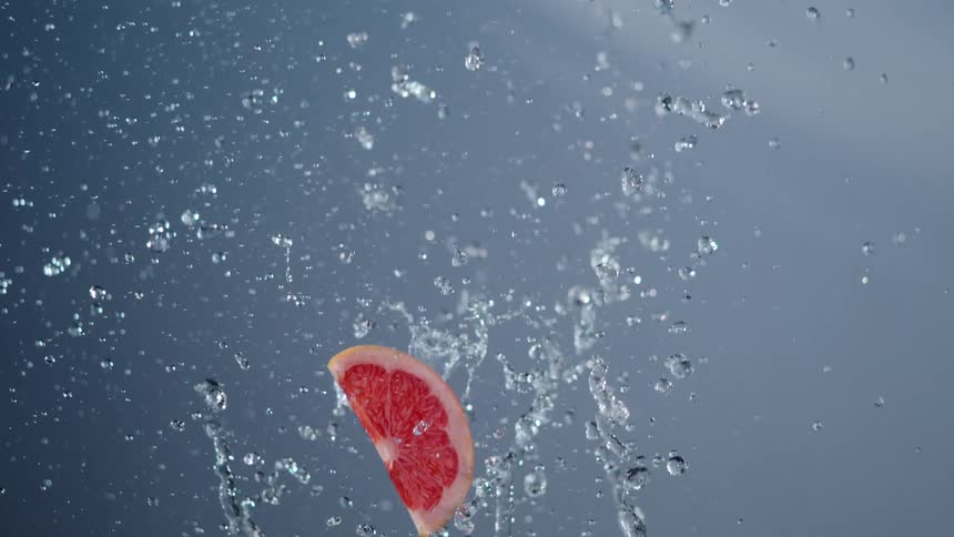 Grapefruit slice falling into water with splashes around it