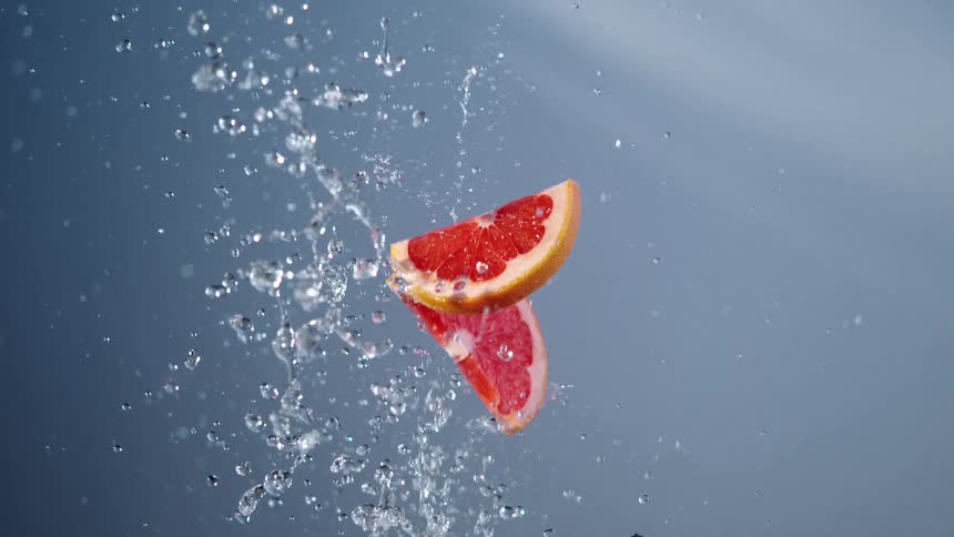 Two slices of grapefruit falling with water splashing on them indoors