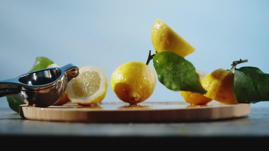 Whole and sliced lemons on a wooden board beside a metal juicer