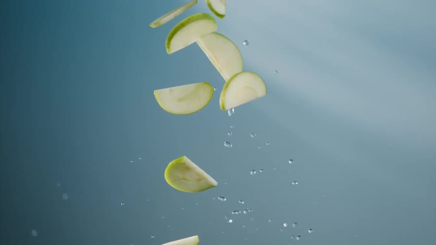 Green apple slices fly into the air and fall