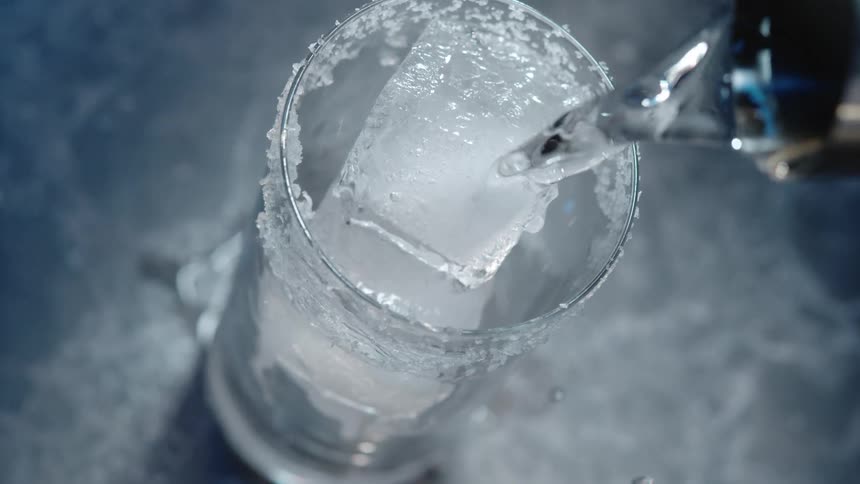 Some alcohol being poured into a glass of ice