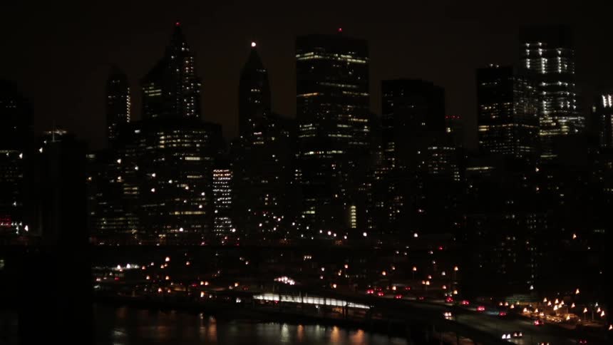 Traffic moves along the coast as lights on metropolitan buildings and towers glow in the darkness