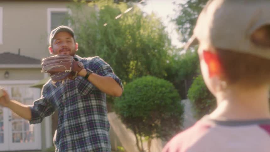 Man throws a baseball to a boy in front yard of home