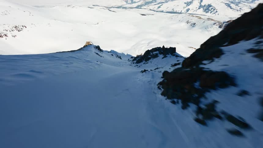 Snowcovered mountain slope with rocky formations and valley in the background