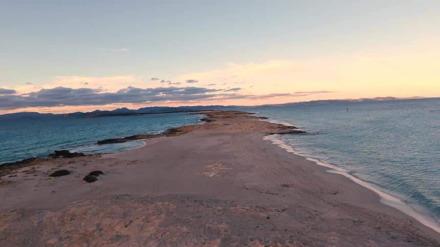 Waves roll in over a strip of land stretching across the water