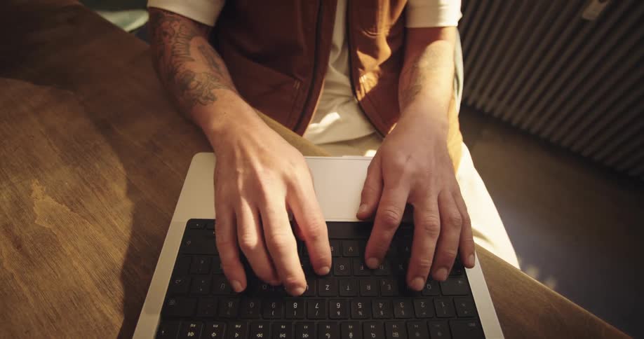 Topdown shot of a person with tattooed arms typing on a laptop