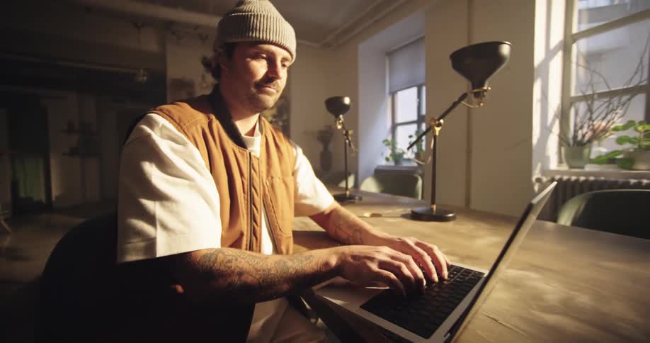 A young man is motivated to work, opens his laptop on a wooden table in a sunlit indoor setting
