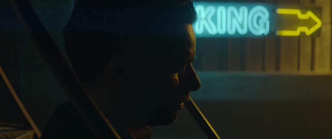 Man sitting in a vehicle with a neon sign in the background at night